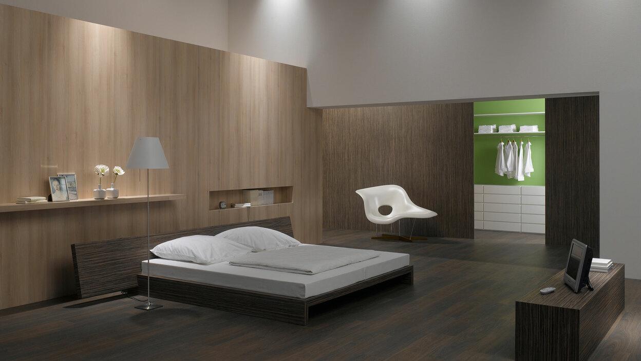 Schlafzimmerimpression von Bett, Nachtisch und Sideboard mit Holzverkleidung an Wand und indirektert Beleuchtung