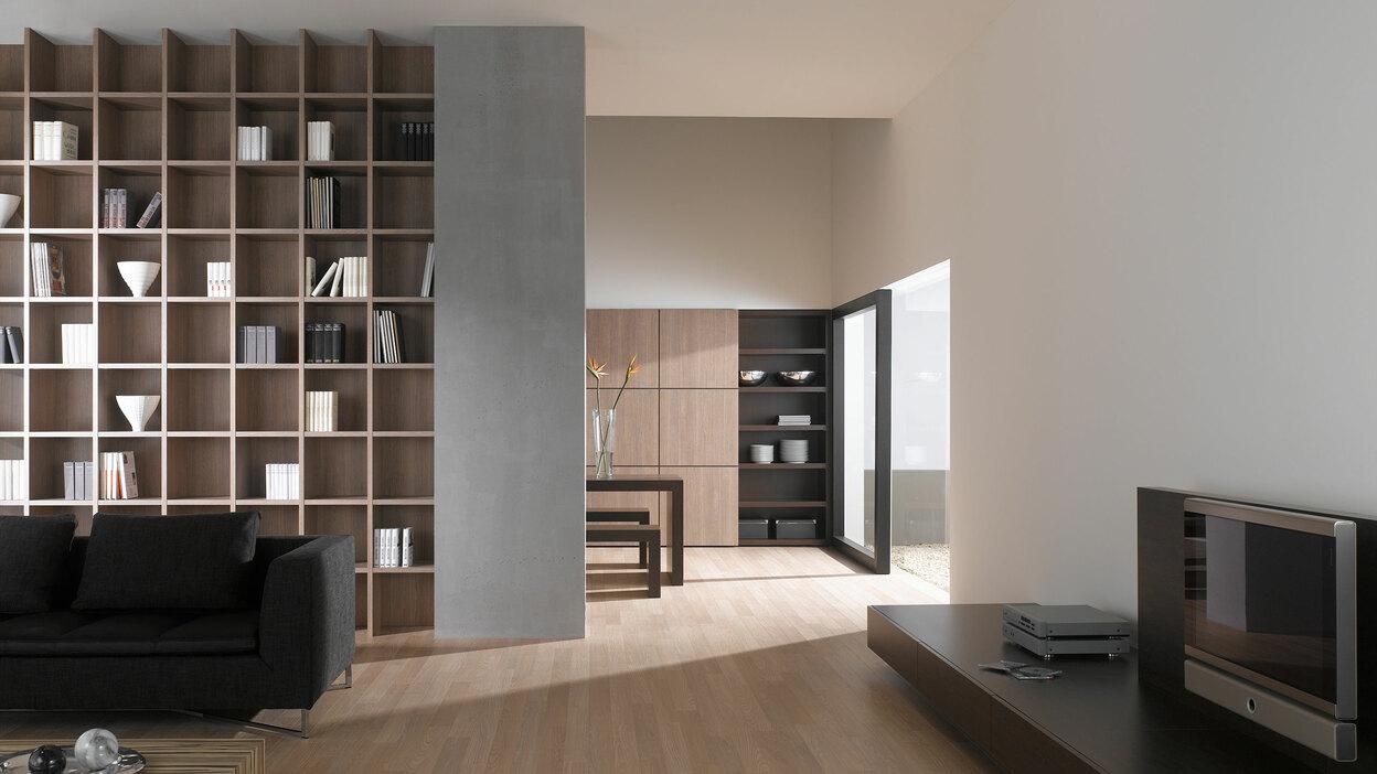 Offene Wohnraumimpression mit Einbauregal für Bücher und Dekoration in Trennwand mit hellem Holzboden
